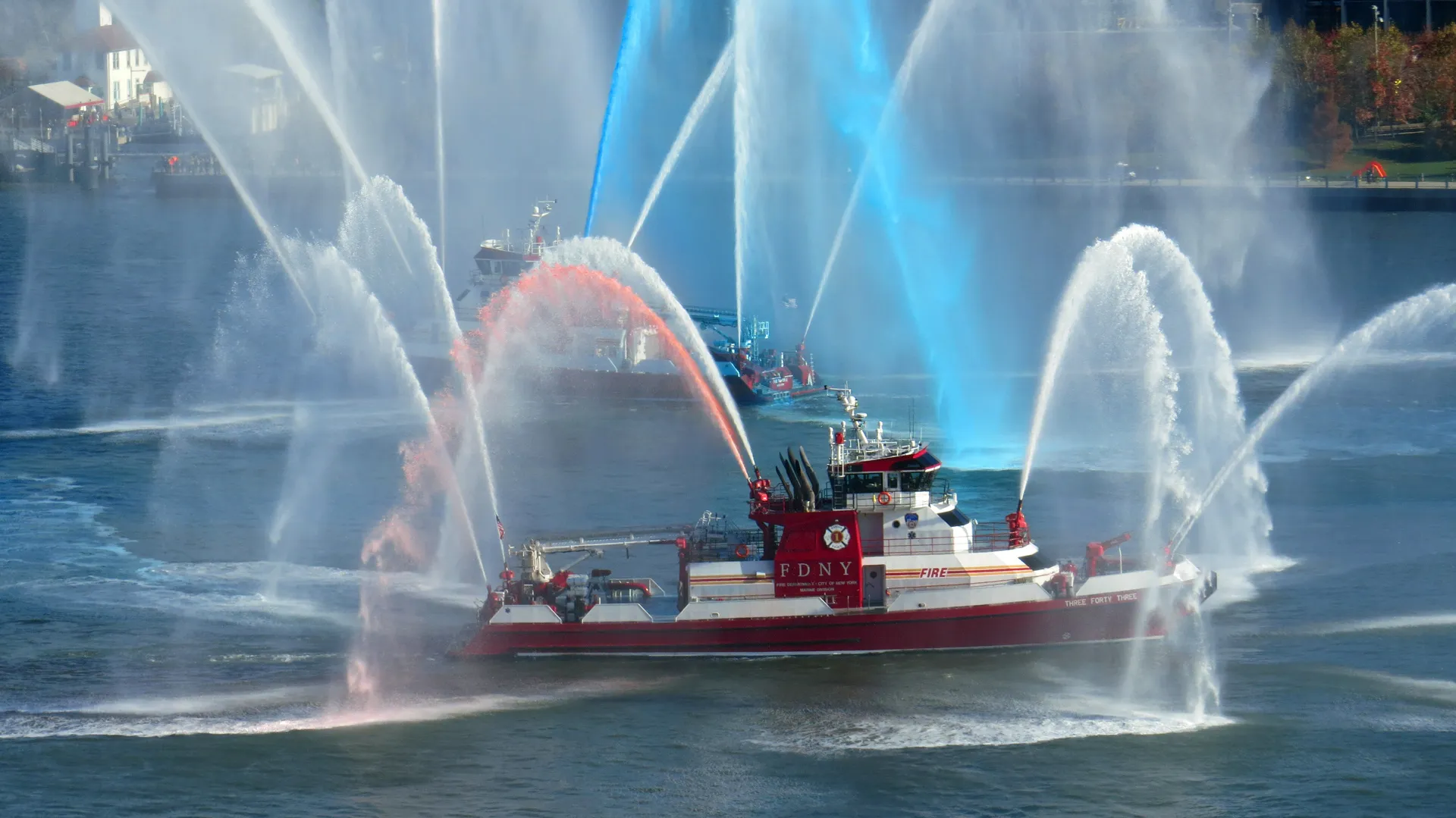 Fireboats spray arcs of white, red, and blue water across a city harbor.